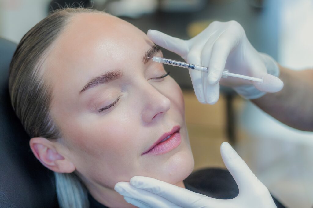 Behandler giver botox ved øjenbrynet med en tynd insulinsprøjte, mens kvinden ligger afslappet med lukkede øjne i behandlingsstolen
