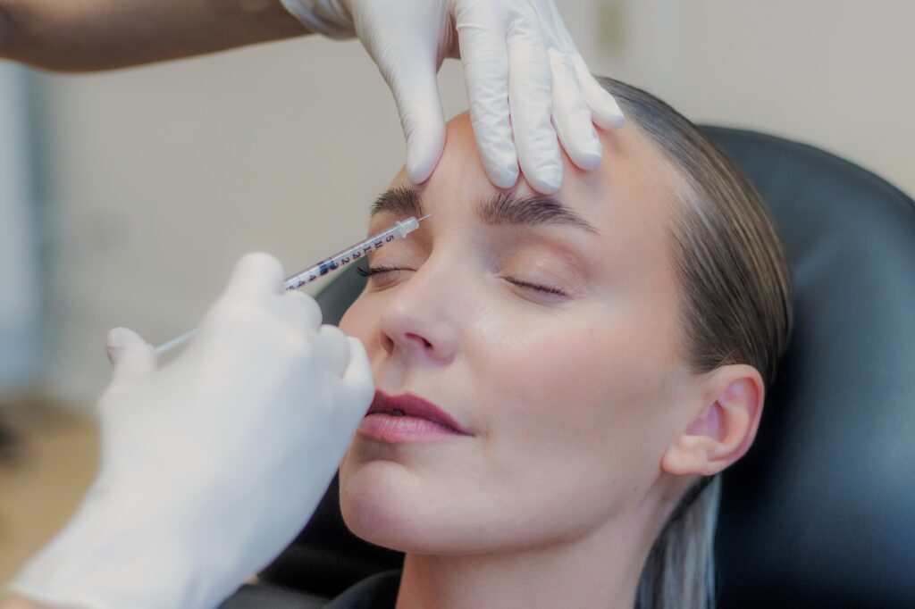 Behandler giver botox mellem øjenbrynene for at blødgøre bekymringsrynken, kvinden ligger med lukkede øjne