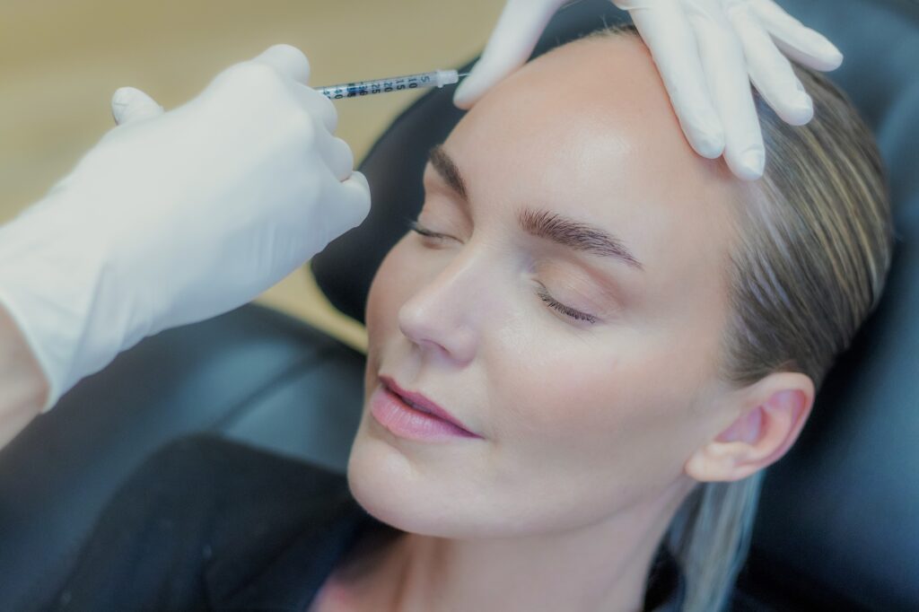 Behandler holder panden udspændt og giver botox i panden med en tynd insulinsprøjte