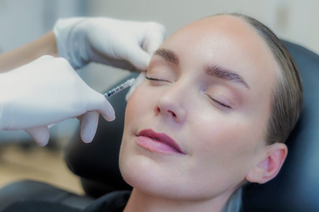 Behandler giver botox ved den ydre øjenkrog mod smilerynker og krågetæer, kvinden ligger med lukkede øjne
