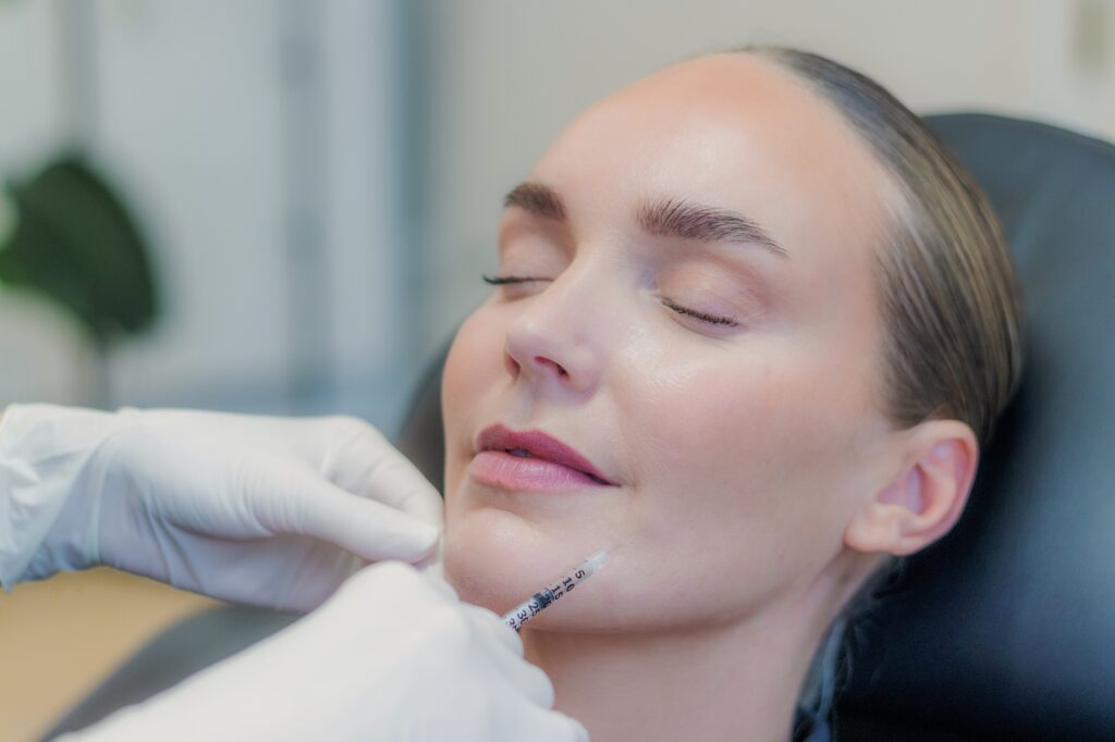 Behandler giver botox i hagen med en tynd insulinsprøjte, kvinden ligger afslappet med lukkede øjne