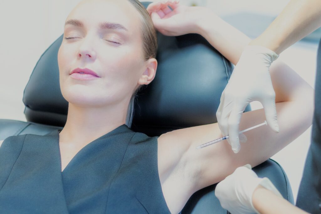Behandler giver botox i armhulen mod kraftig svedtendens, kvinden ligger med armen hævet over hovedet