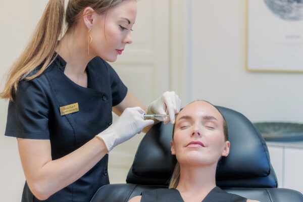 Kosmetisk sygeplejerske giver botox i panden, kvinden ligger med lukkede øjne i den sorte behandlingsstol
