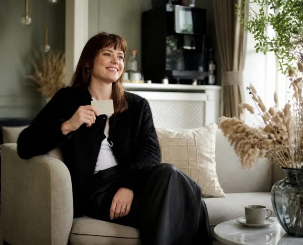 Kvinde i sofa smiler og holder NOMO VIP-kort